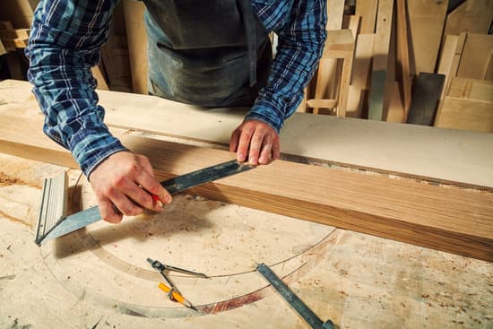 Craftsman Measuring and Cutting Wood in Workshop Carpenter measuring and cutting a wood board on a workbench in a woodworking shop.