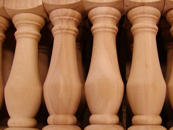 Up close view of four large turned wood balusters with square top and bottom.