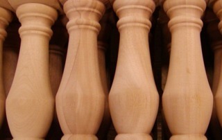 Close-up of four large turned wood balusters featuring square tops and bottoms, designed for architectural applications.