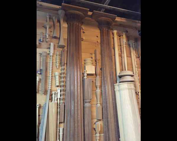 Wall display of various wooden balusters, newel posts, posts and columns that features a set of walnut pilasters.