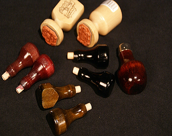 Nine custom wooden stamp handles. Two have a clear finish, three have a mahogany stain, two with a black paint, and two a walnut stain.