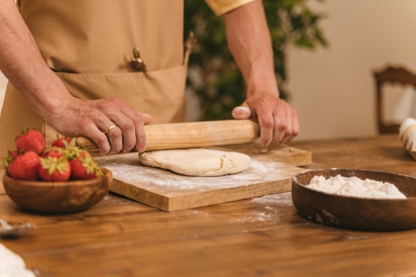 Man Using a Wood Rolling Pin to Flatten Dough A man rolling out dough with a wood rolling pin on a floured surface.