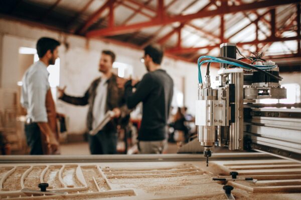 A wood CNC machine in operation, with three people discussing machining services in the background.