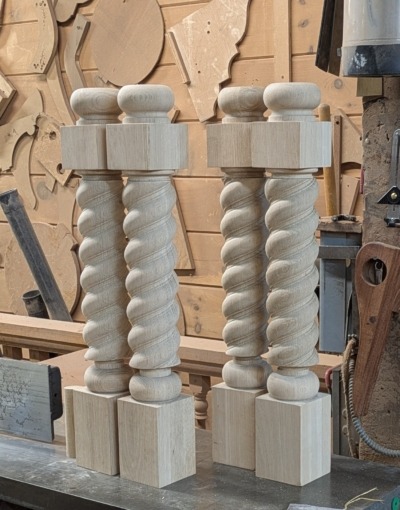 Custom Twisted White Oak Table Legs – Bulk and Small Order Wood Turnings Four custom twisted white oak table legs with square tops and bases, displayed in a woodworking shop setting.