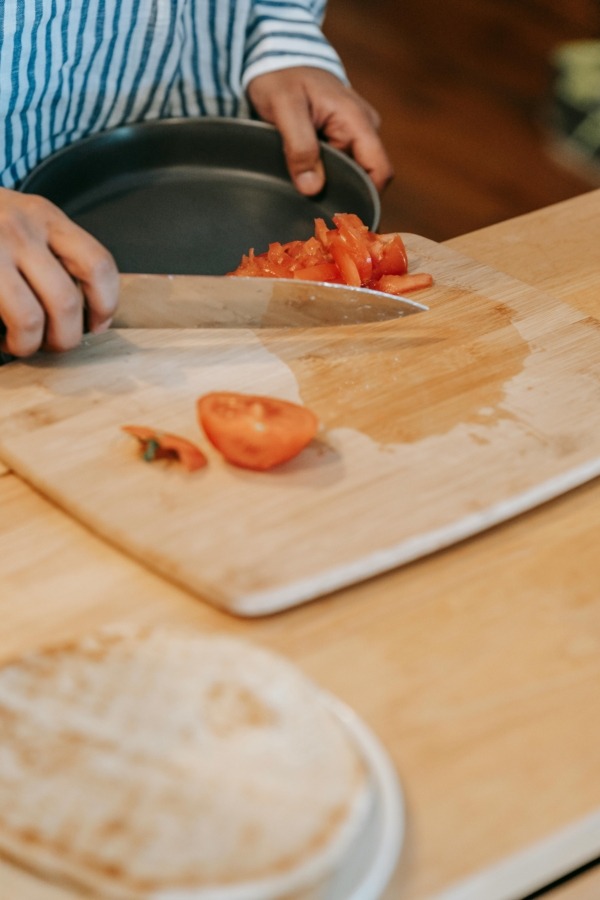 Person chopping fresh tomatoes on a hardwood cutting board made from light maple wood.