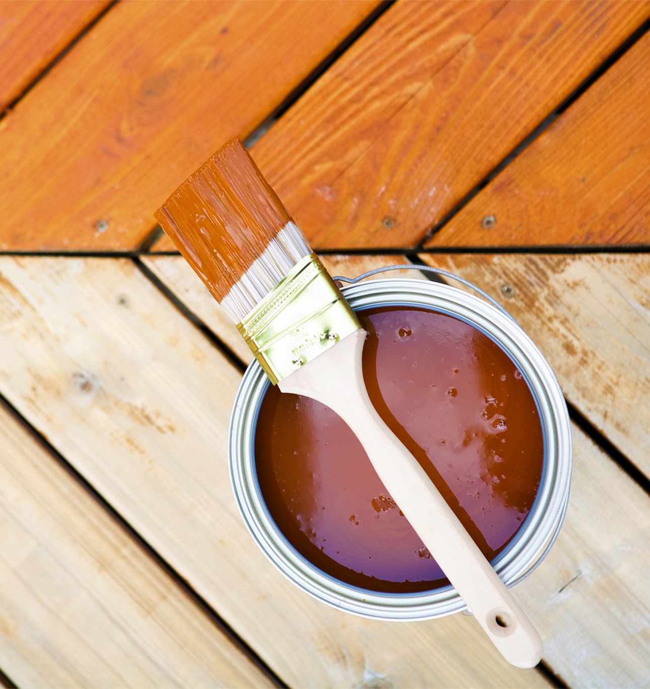 Staining or painting pressure treated wood after drying Paintbrush resting on a can of brown wood stain beside a partially stained pressure treated deck board. Shows before and after of applying stain or paint on pressure treated wood.
