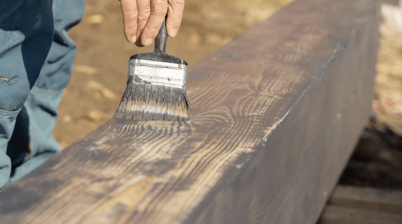Staining pressure treated wood after drying Close-up of a person applying dark wood stain to a pressure treated timber with a wide brush. The surface shows partial absorption of the stain on dried wood.