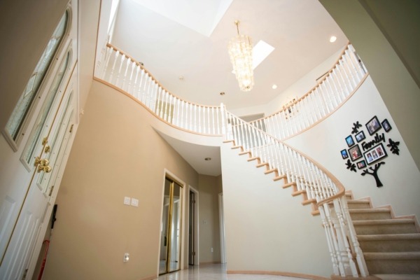 Curved wood staircase with white turned spindles, natural wood handrail, and neutral wall tones in a modern entryway.