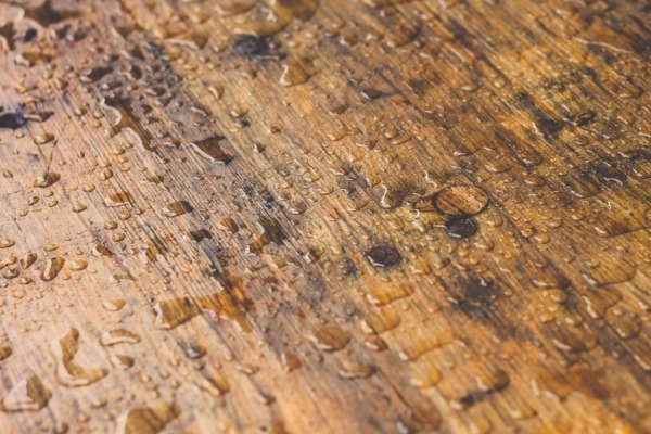 Close-up of water droplets on a stained wood surface showing signs of moisture damage.