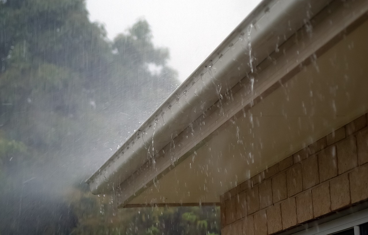 Overflowing Gutter During Rainfall Overflowing gutter spilling water during heavy rain near porch roof.