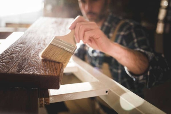 Close-up of polyurethane being applied to a smooth wooden board with a natural bristle brush.