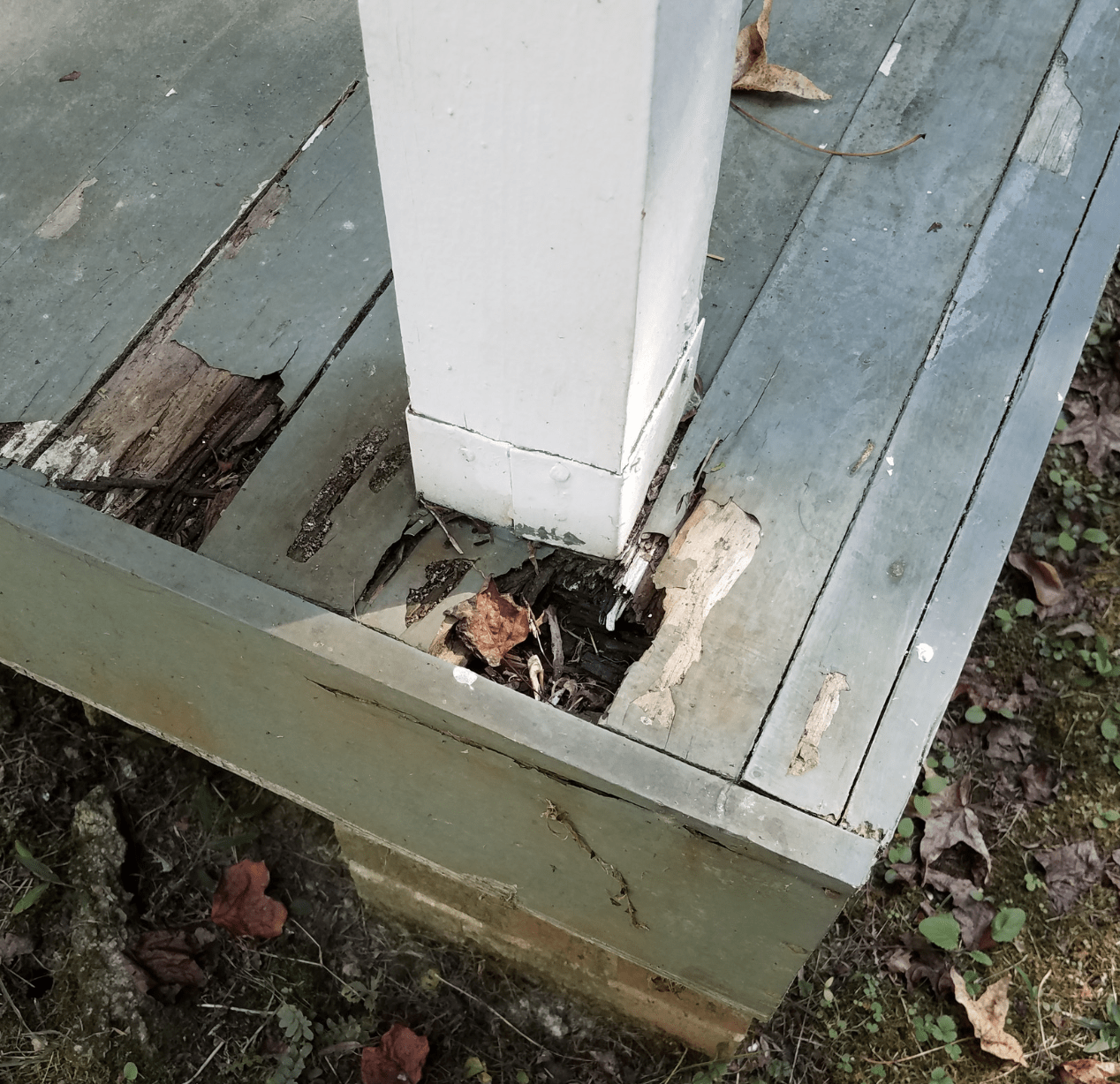 Rotted Wood Porch Column with Moisture Damage Rotted wood porch column base showing peeling paint and water damage.