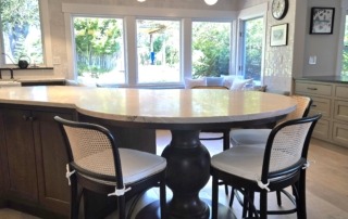 Wood Pedestal Base Supporting Kitchen Island Overhang Stained wooden pedestal base supporting a rounded kitchen island overhang with bar stools in a bright modern kitchen.z